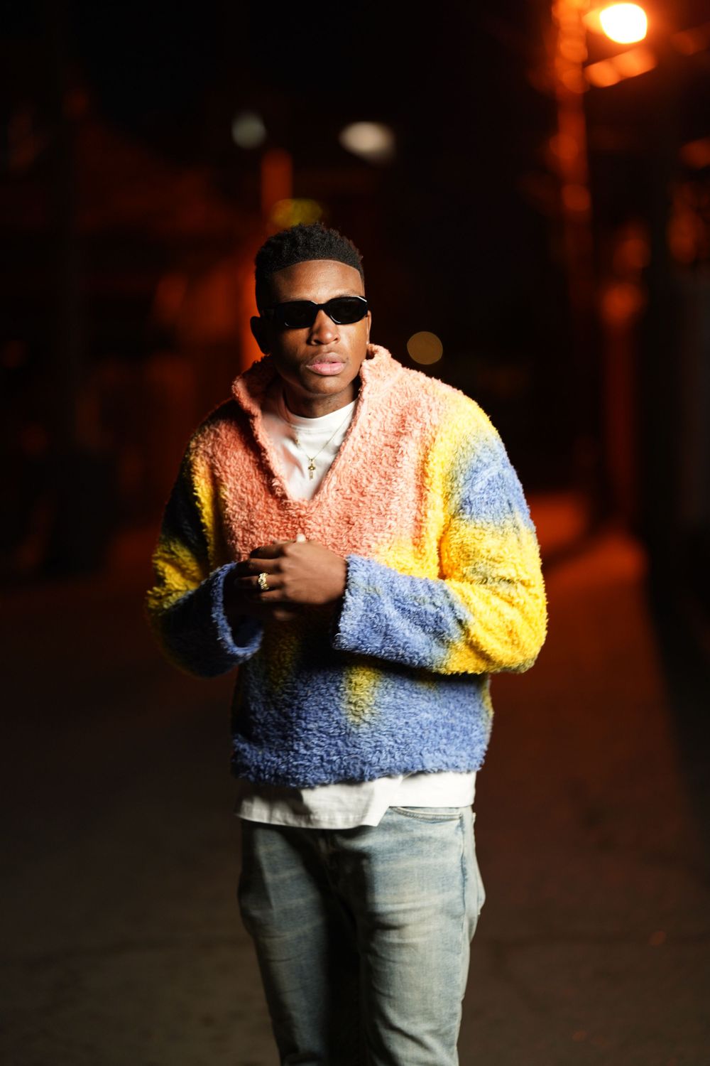Person in a tricolor fuzzy sweater and jeans photographed against dark urban background.