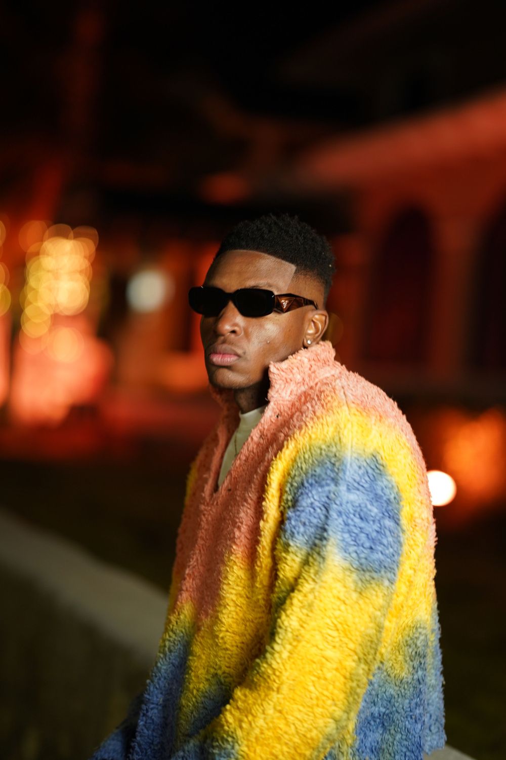 A portrait at night featuring a colorful multicolored fleece sweater and sunglasses.