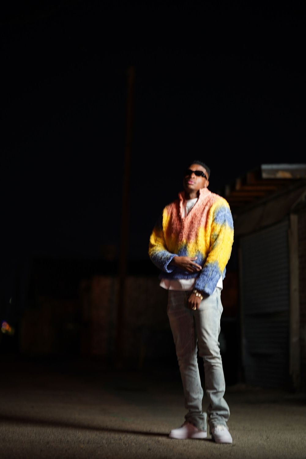 Person wearing a colorful sweater and jeans posing in dramatic nighttime lighting.
