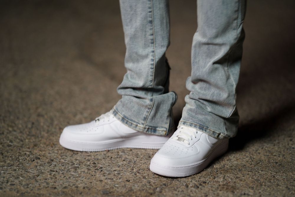 White sneakers and light blue jeans shown from below in a dimly lit setting.