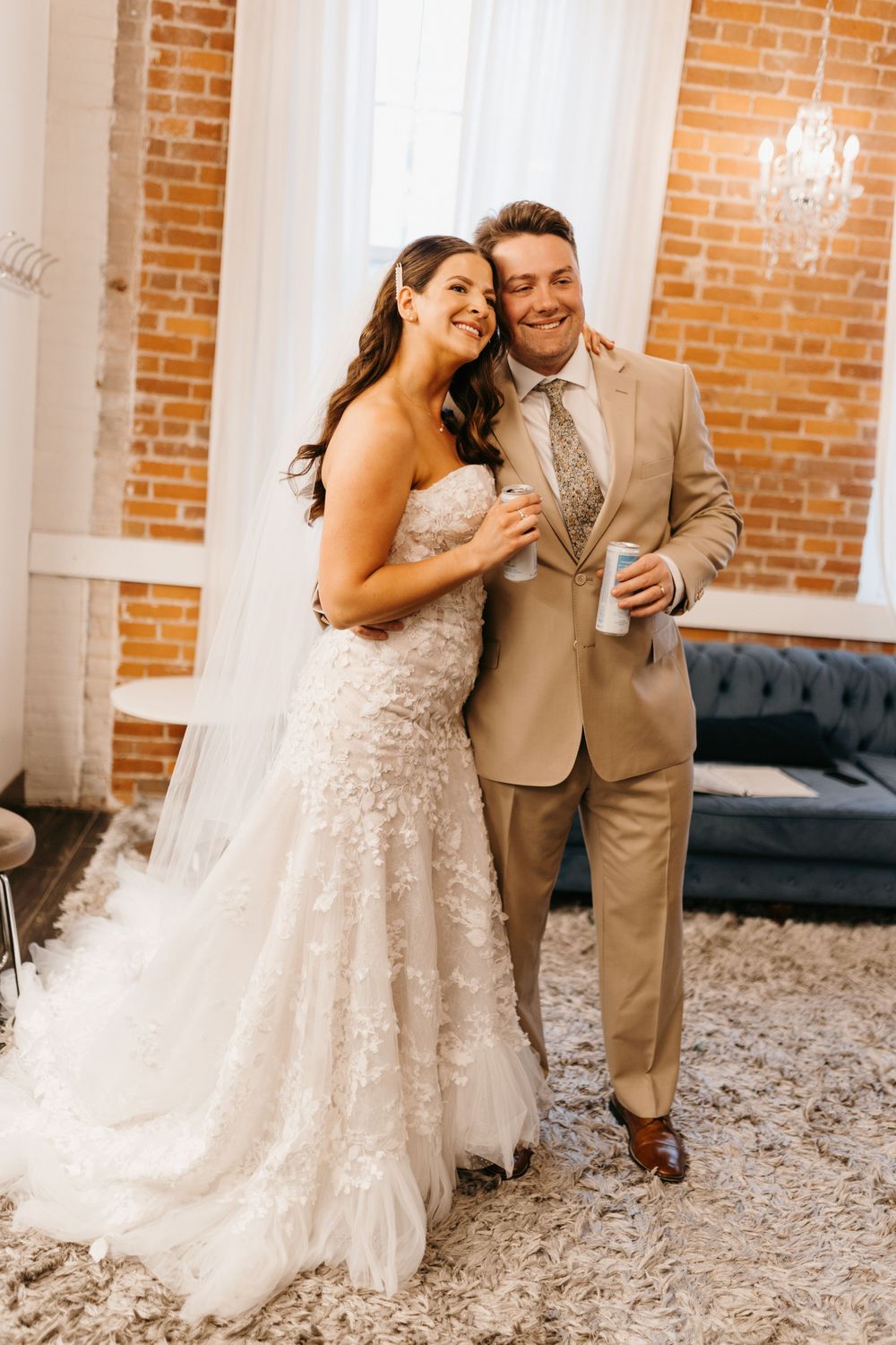 Smiling bride and groom pose together in elegant brick-walled bridal suite after ceremony.