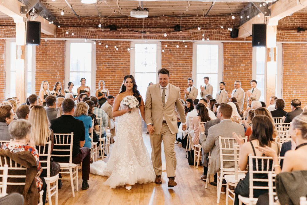 Newlyweds walk joyfully down aisle after ceremony in rustic brick wedding venue.