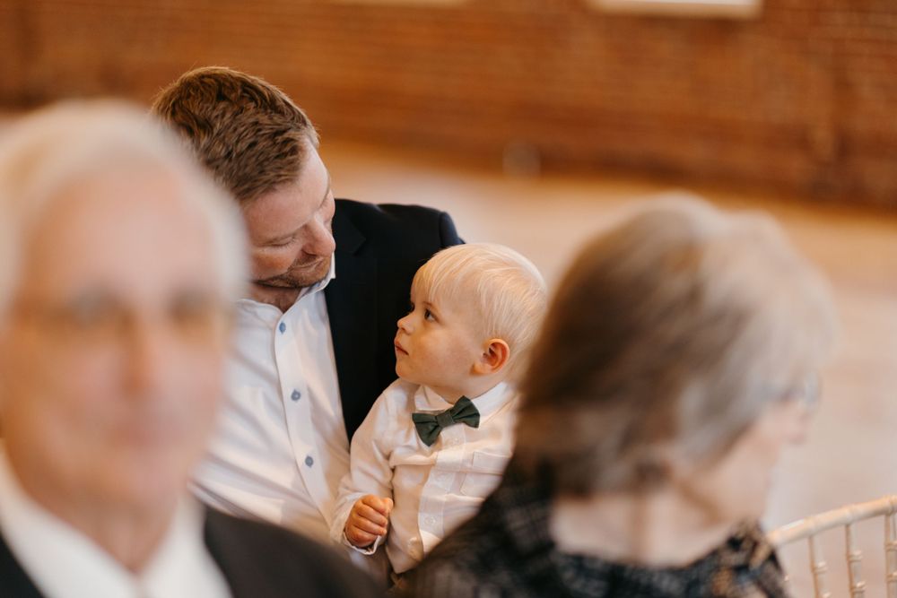 A smiling father holds his young son in a bow tie during a wedding ceremony.