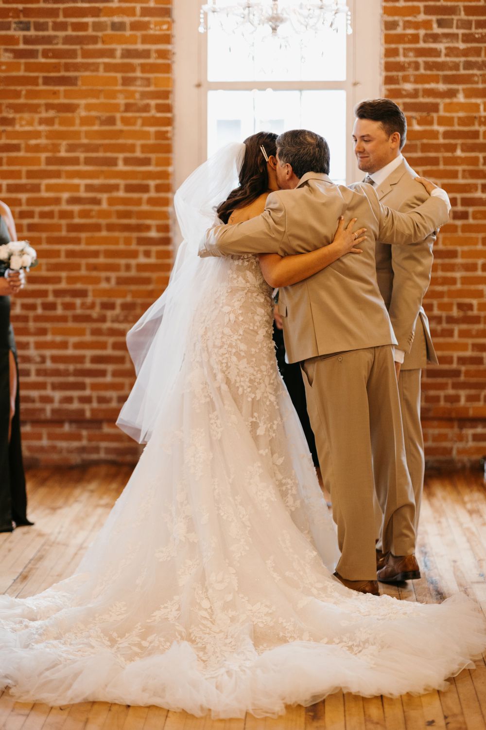 Bride and groom share first hug at altar in lace gown and tan suit at wedding.