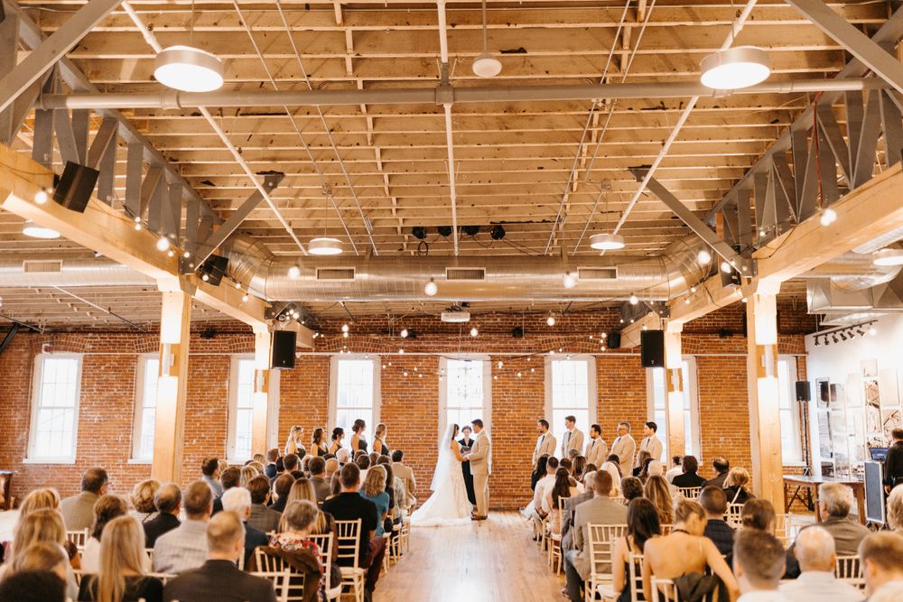 Wedding ceremony in progress inside rustic brick venue with wooden ceiling and warm lighting.