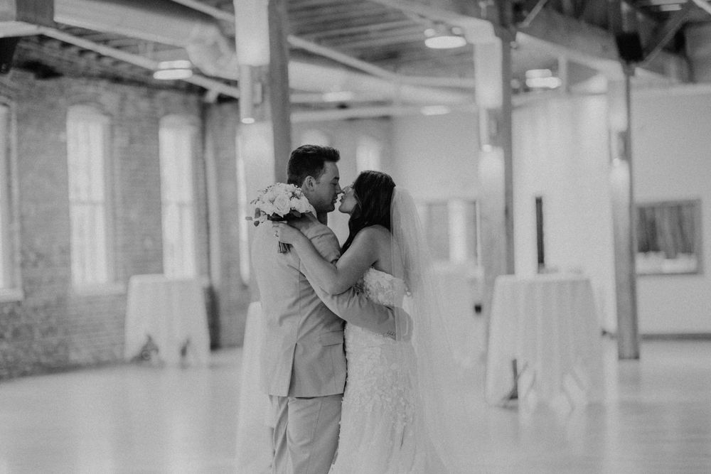 Black and white photo of newlyweds embracing tenderly in spacious wedding reception hall.