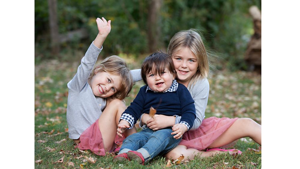 Three children laughing and playing together while sitting on autumn leaves.