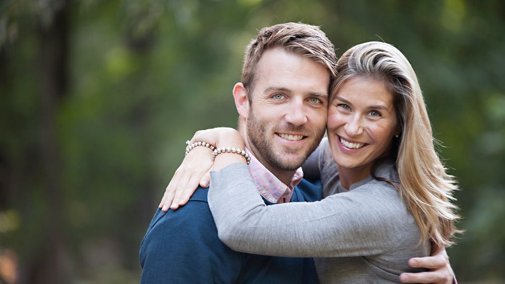 Couple embracing outdoors with natural greenery in the background.