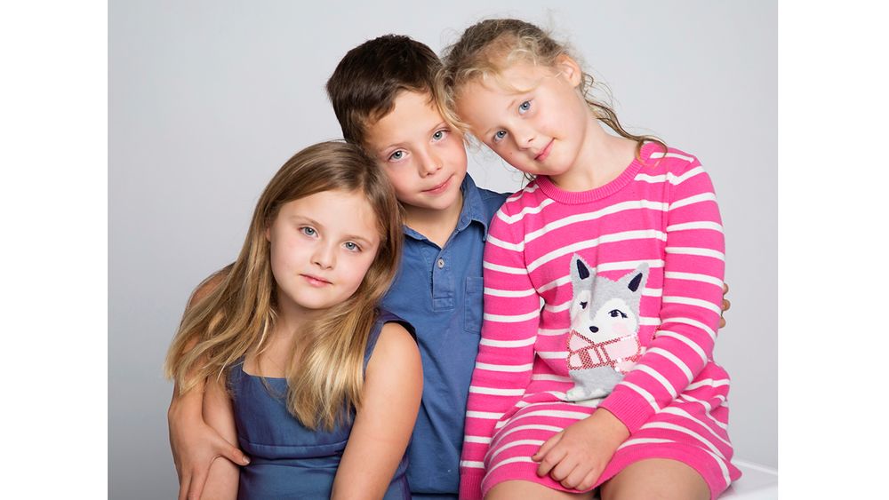 Three siblings in casual attire pose together against a light gray studio backdrop.