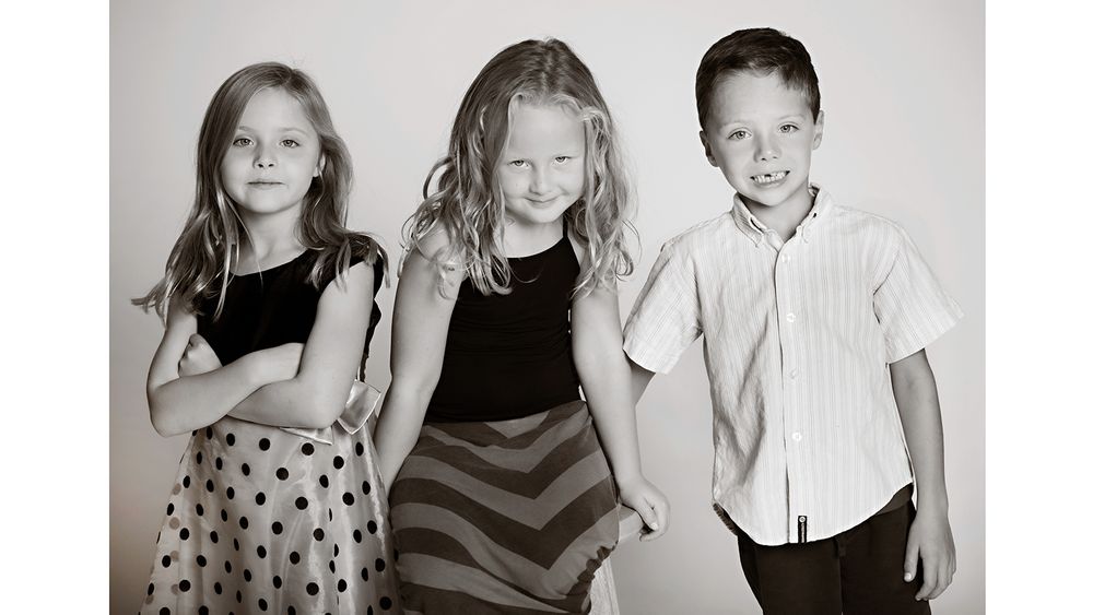 Three young children pose together in a black and white portrait with polka dots and stripes.