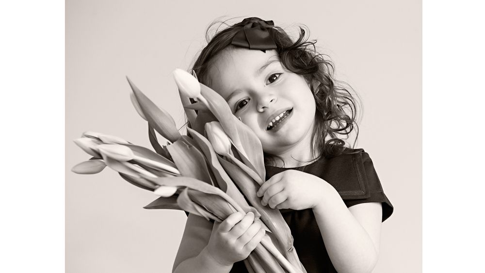 Black and white portrait of someone holding fresh tulips and smiling at the camera.