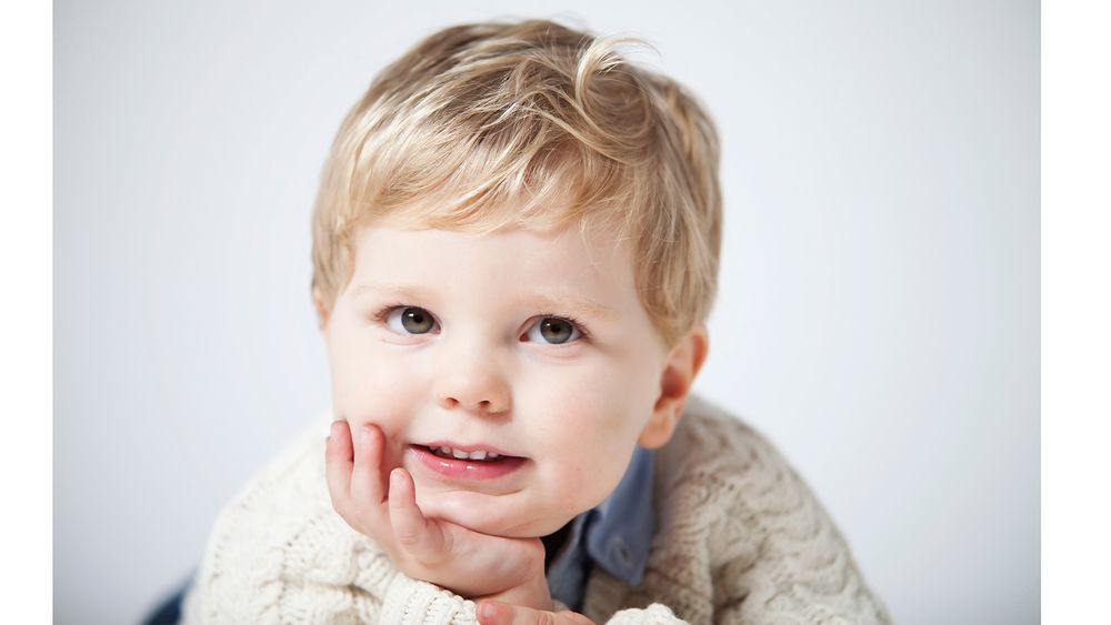 Close-up portrait of a smiling toddler in a cream sweater against a light background.
