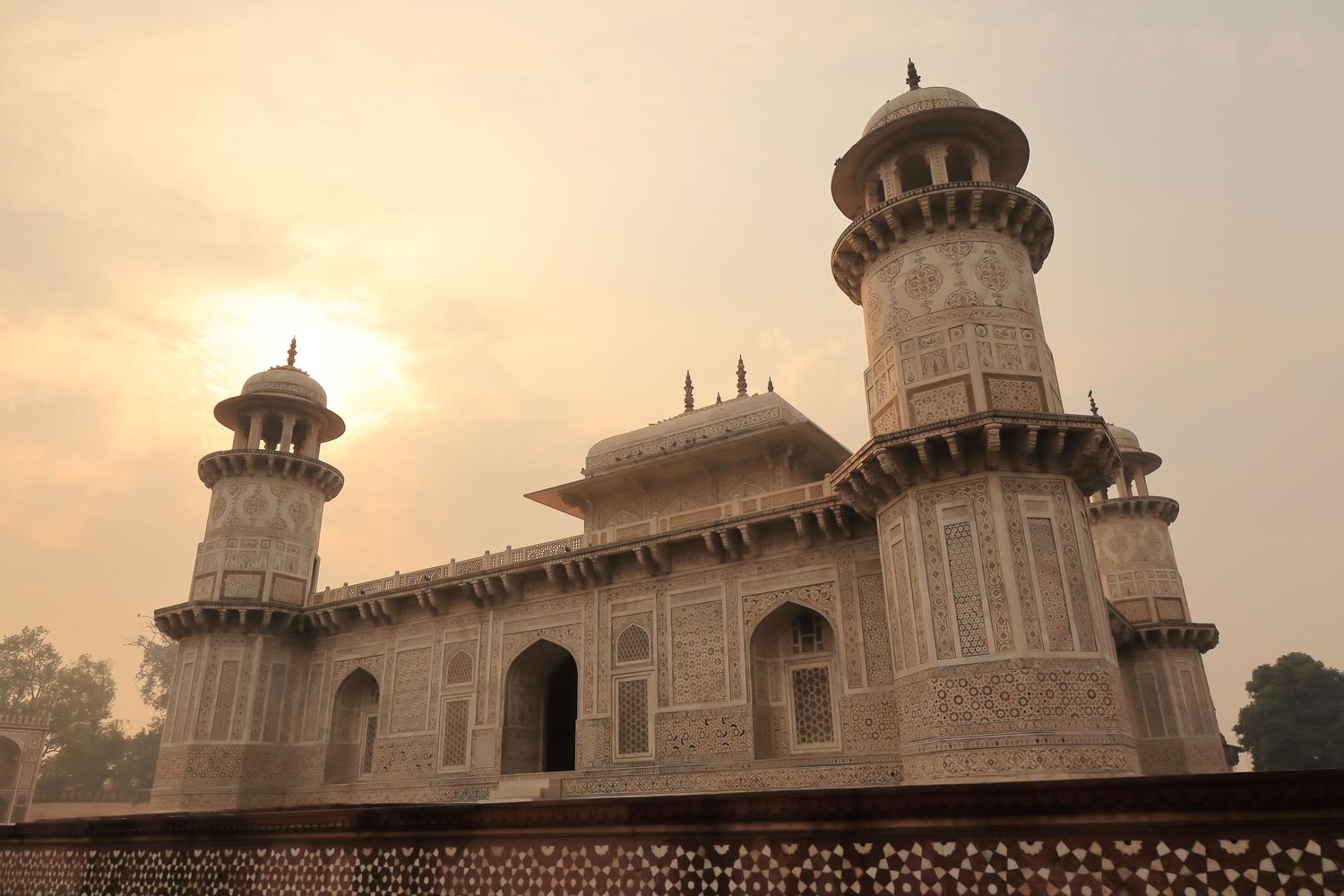 Baby Taj tomb with white domed towers and arched entrance glowing in golden sunset light.
