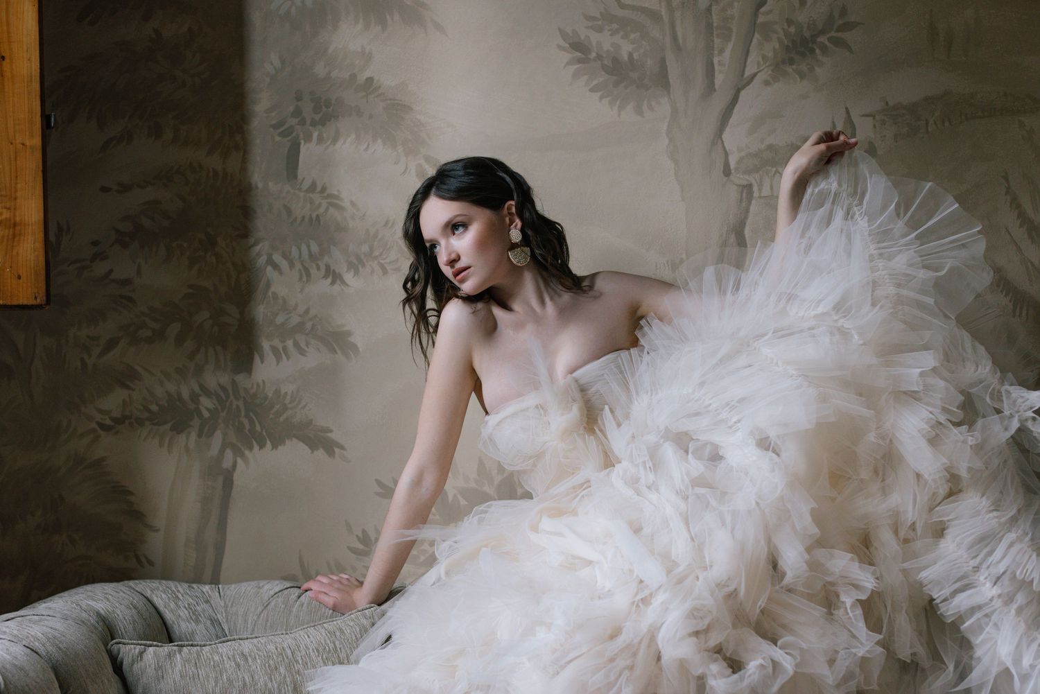 Ethereal scene with flowing white tulle gown against a misty grey wall mural.