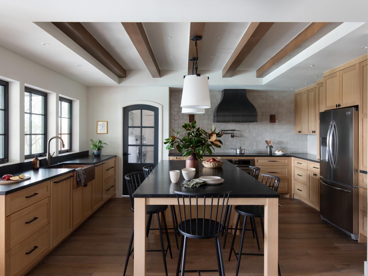 Modern kitchen with wooden cabinets, exposed beams, and black accents featuring an island with seating.