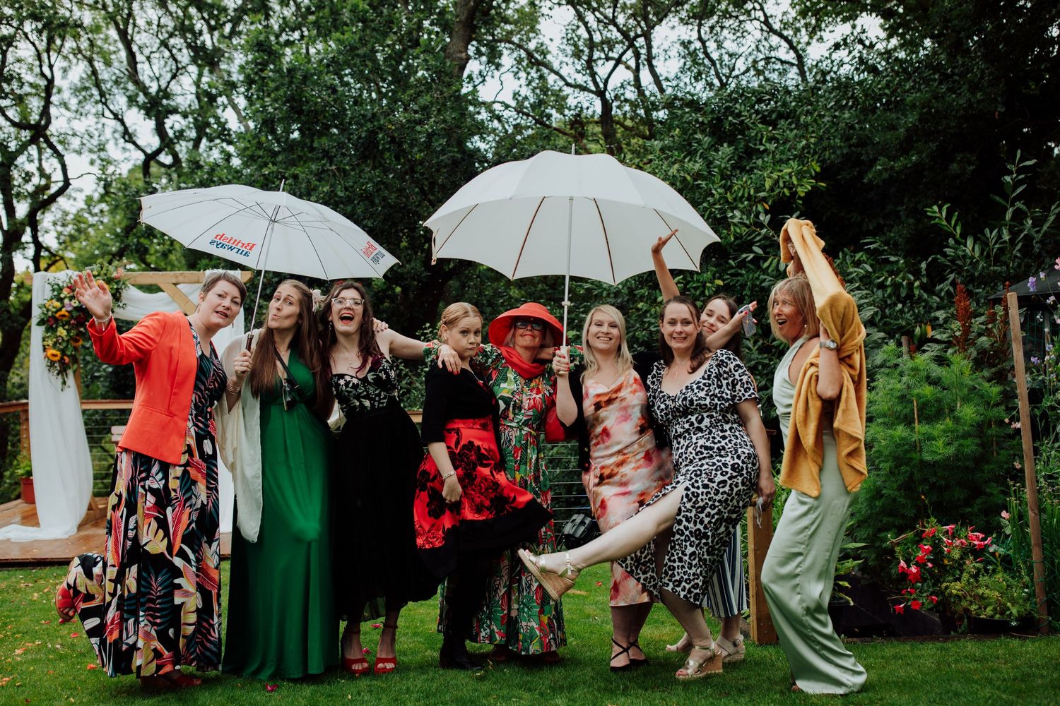 A group celebrating outdoors with white umbrellas and colorful dresses in a garden setting.