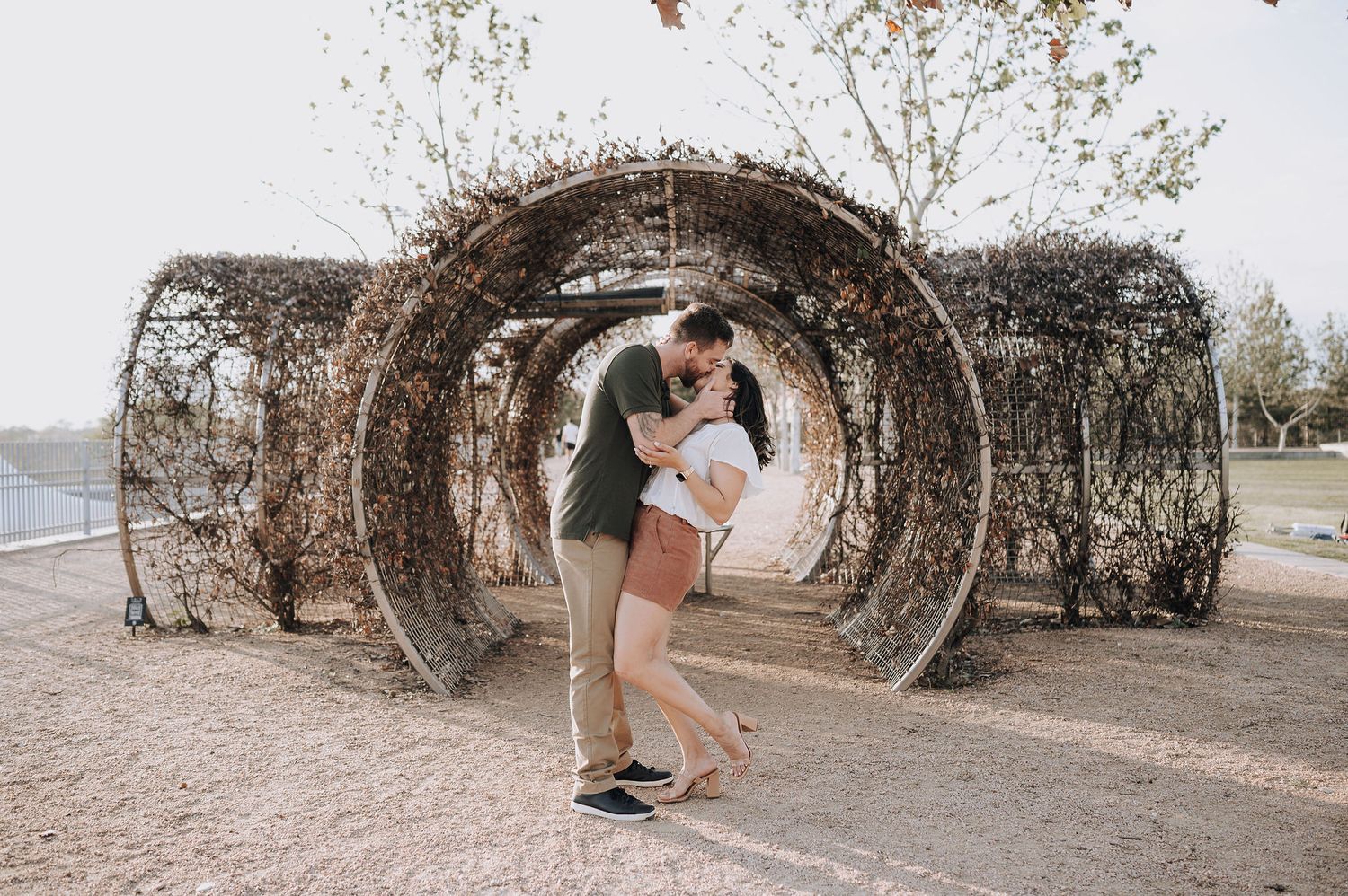 A couple sharing an intimate moment inside a decorative tunnel structure outdoors.