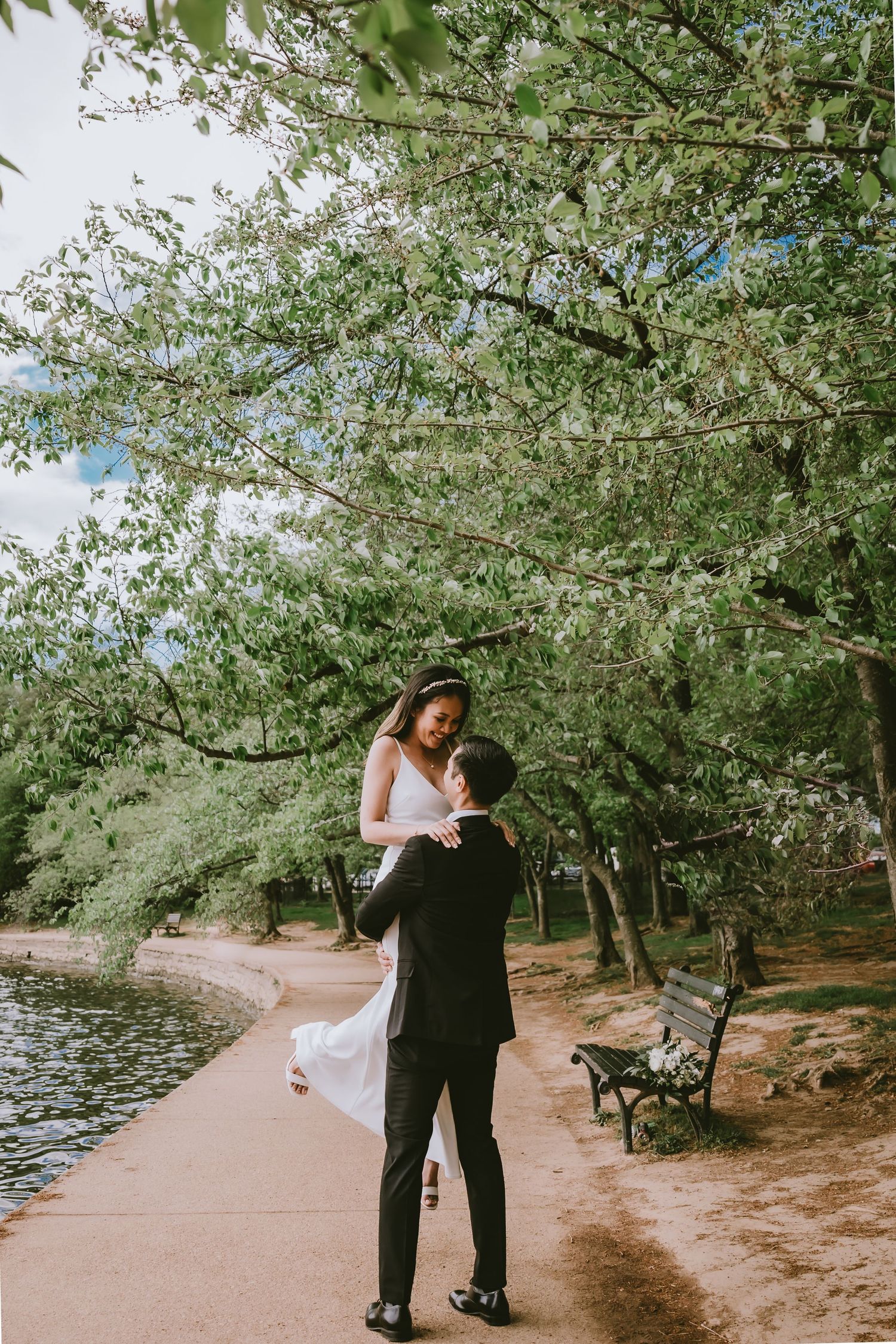 A couple shares a romantic moment by a lakeside path under blooming spring trees.