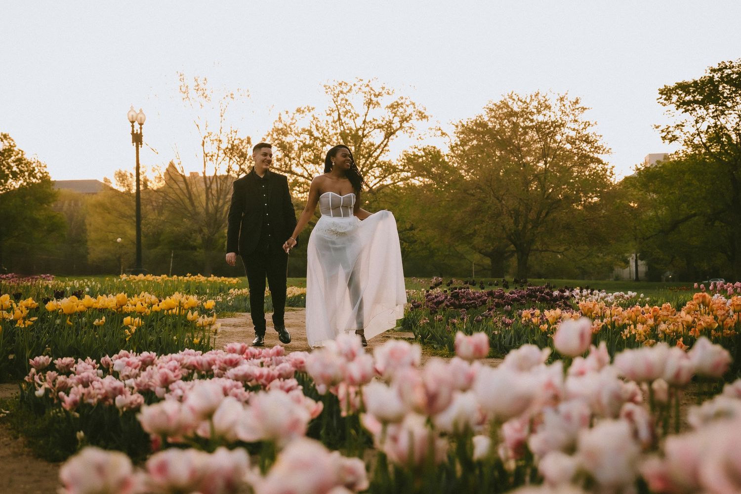 A couple stands in a vibrant tulip garden at sunset surrounded by pink and yellow blooms.
