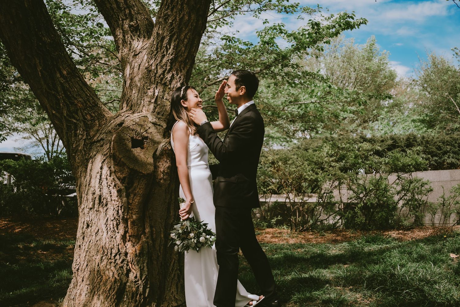 A couple shares an intimate moment against a large tree trunk in a spring garden setting.
