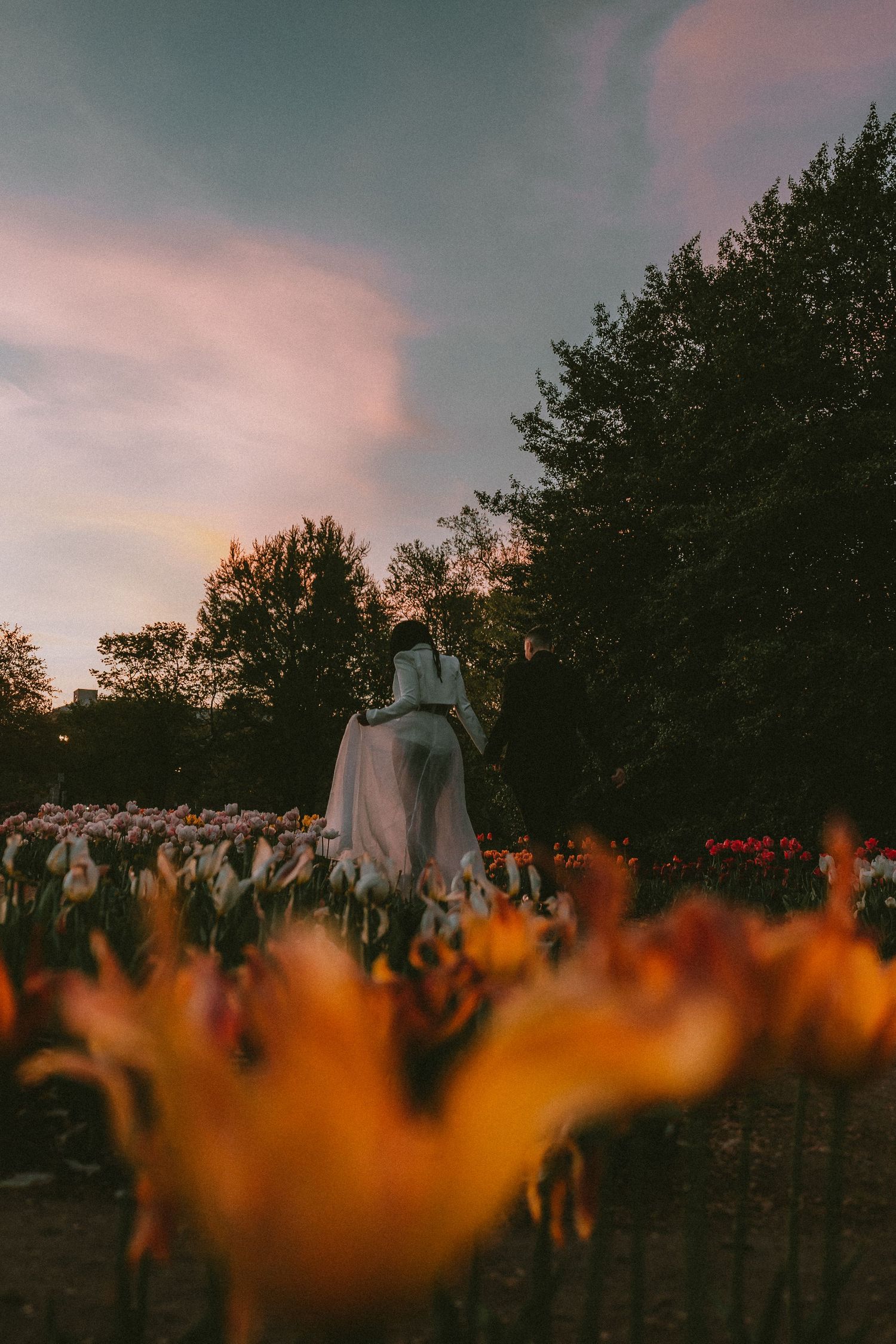 A couple photographed from behind stands among colorful tulip fields at dusk.