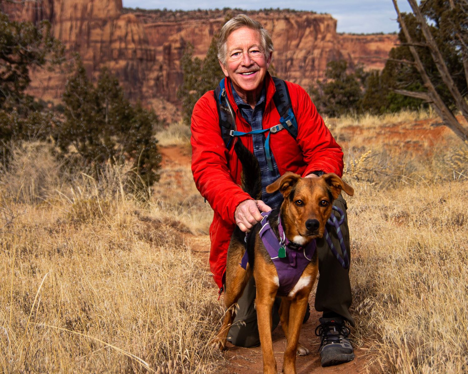A pet portrait photo of a man in a red jacket hugging his dog for the website WhiteFlamingoPhotos.com