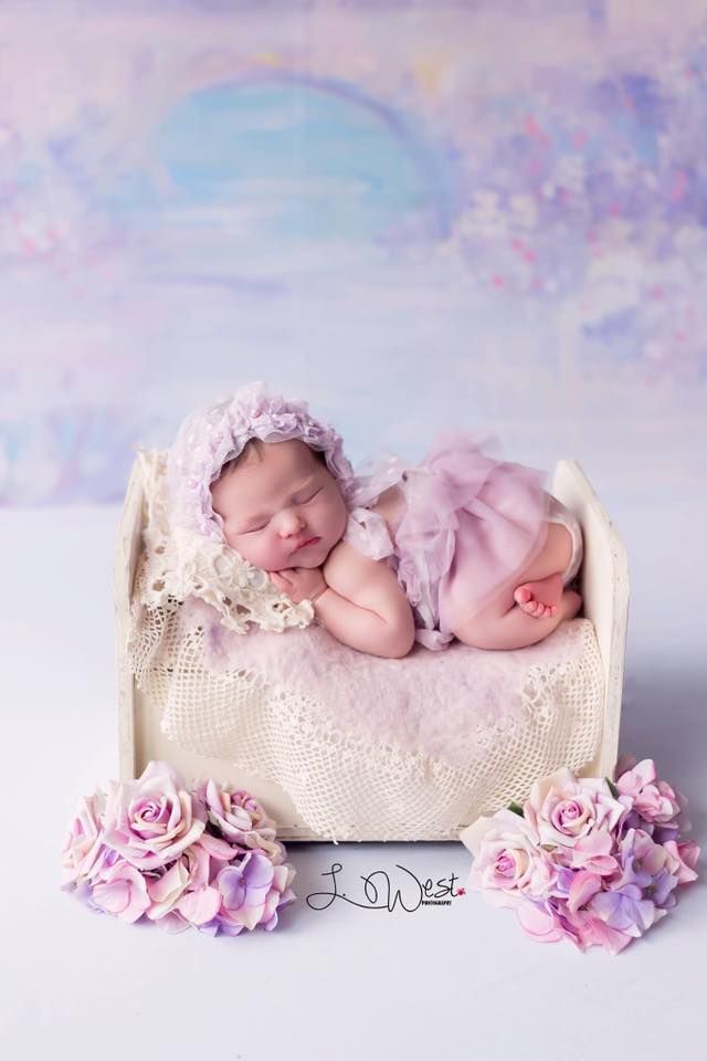 Sleeping newborn in pink dress lying in white basket with pink roses.