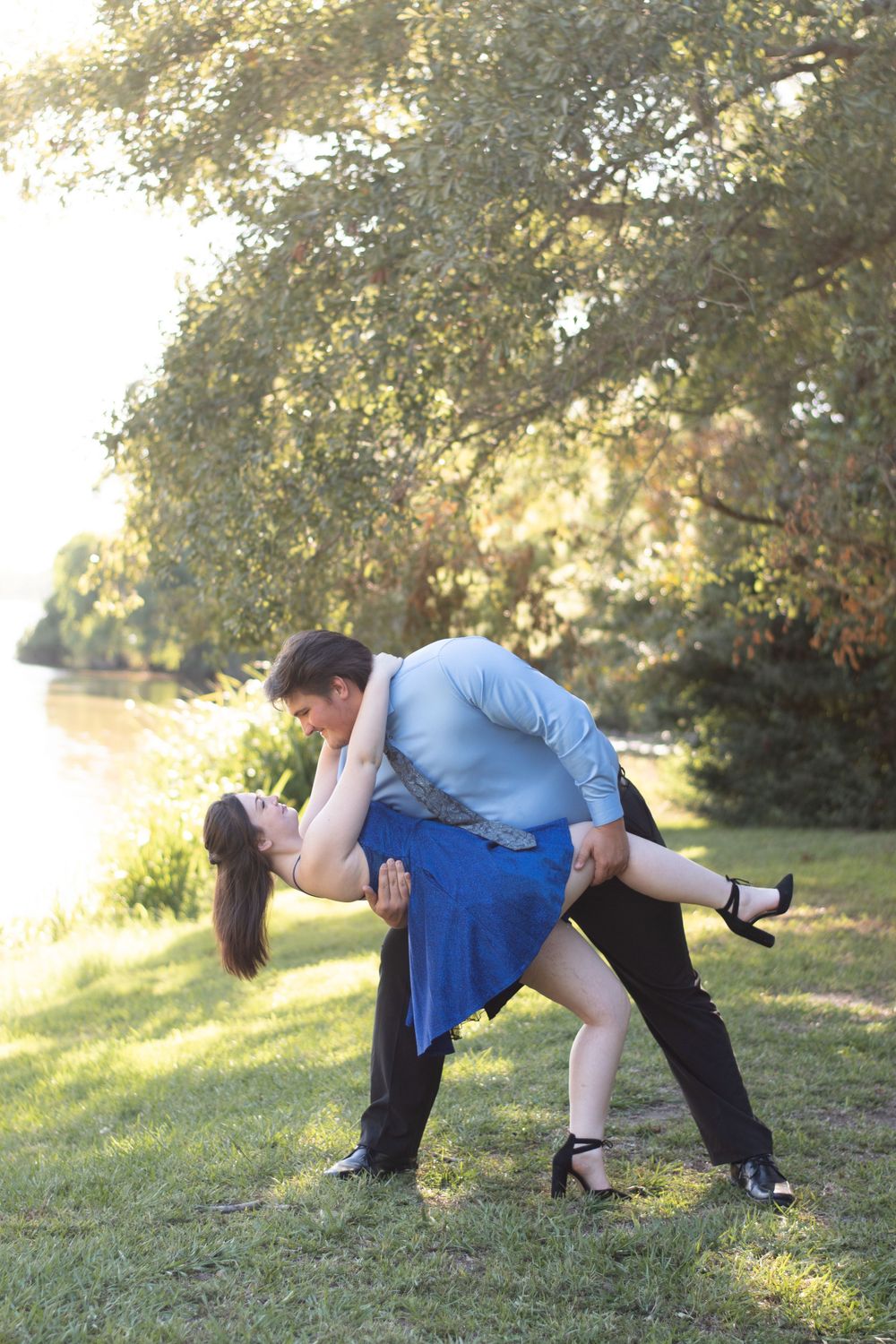 Romantic couple in formal attire dancing in a sunlit garden setting.