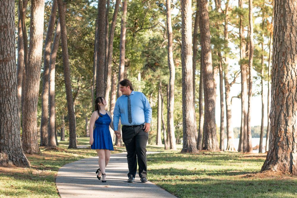 A couple walks hand in hand along a tree-lined path on a sunny afternoon.