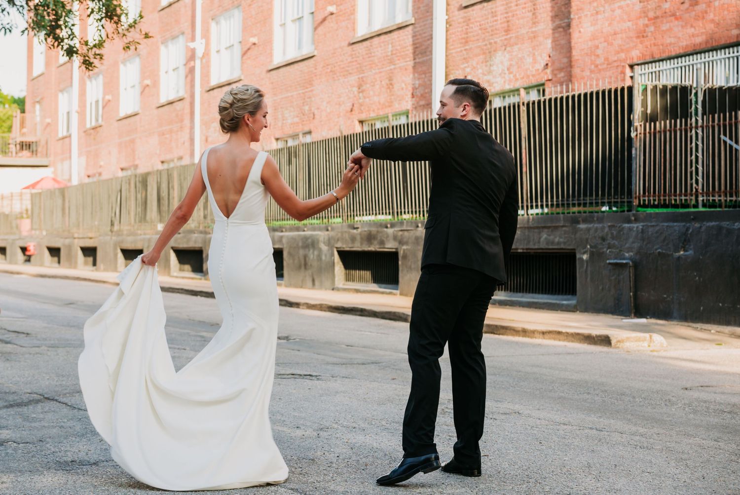 A couple shares a dancing moment on an urban street, with the bride wearing a flowing white dress with open back.
