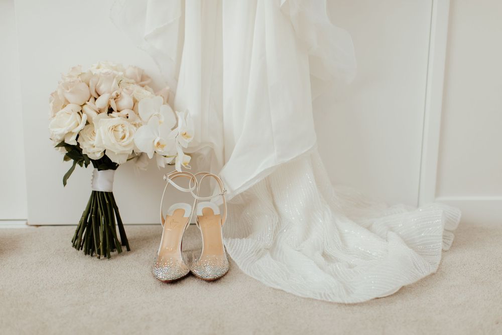 Elegant bridal details with white roses bouquet and crystal-embellished heels against wedding dress.