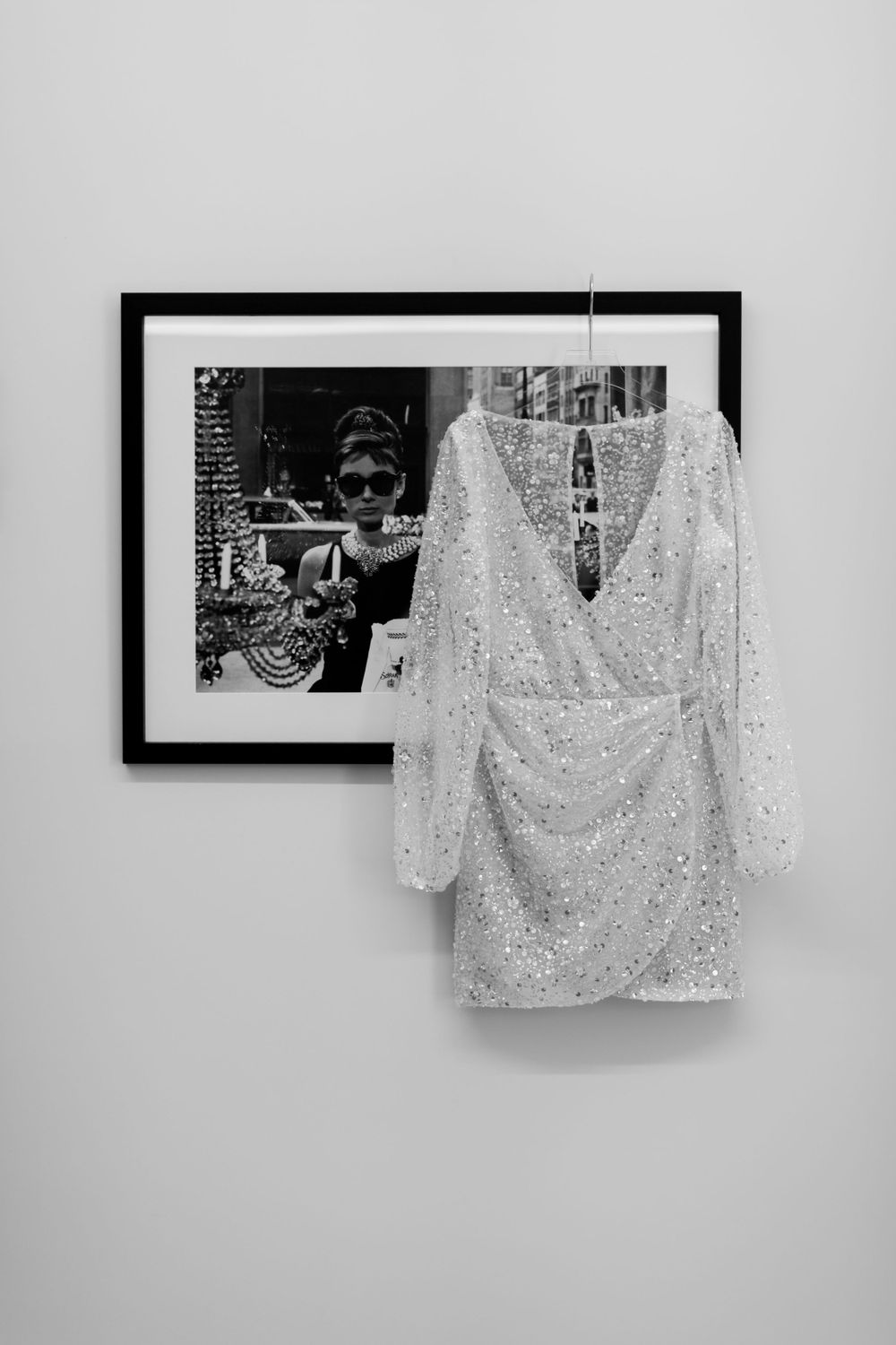 A sparkly white sequined dress hangs against a wall with a framed black and white photograph.