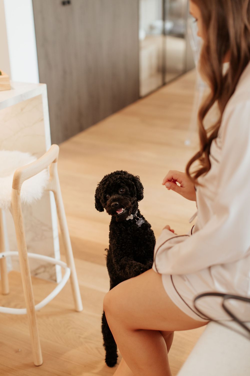 Woman in white robe plays with small black dog on hardwood floor.