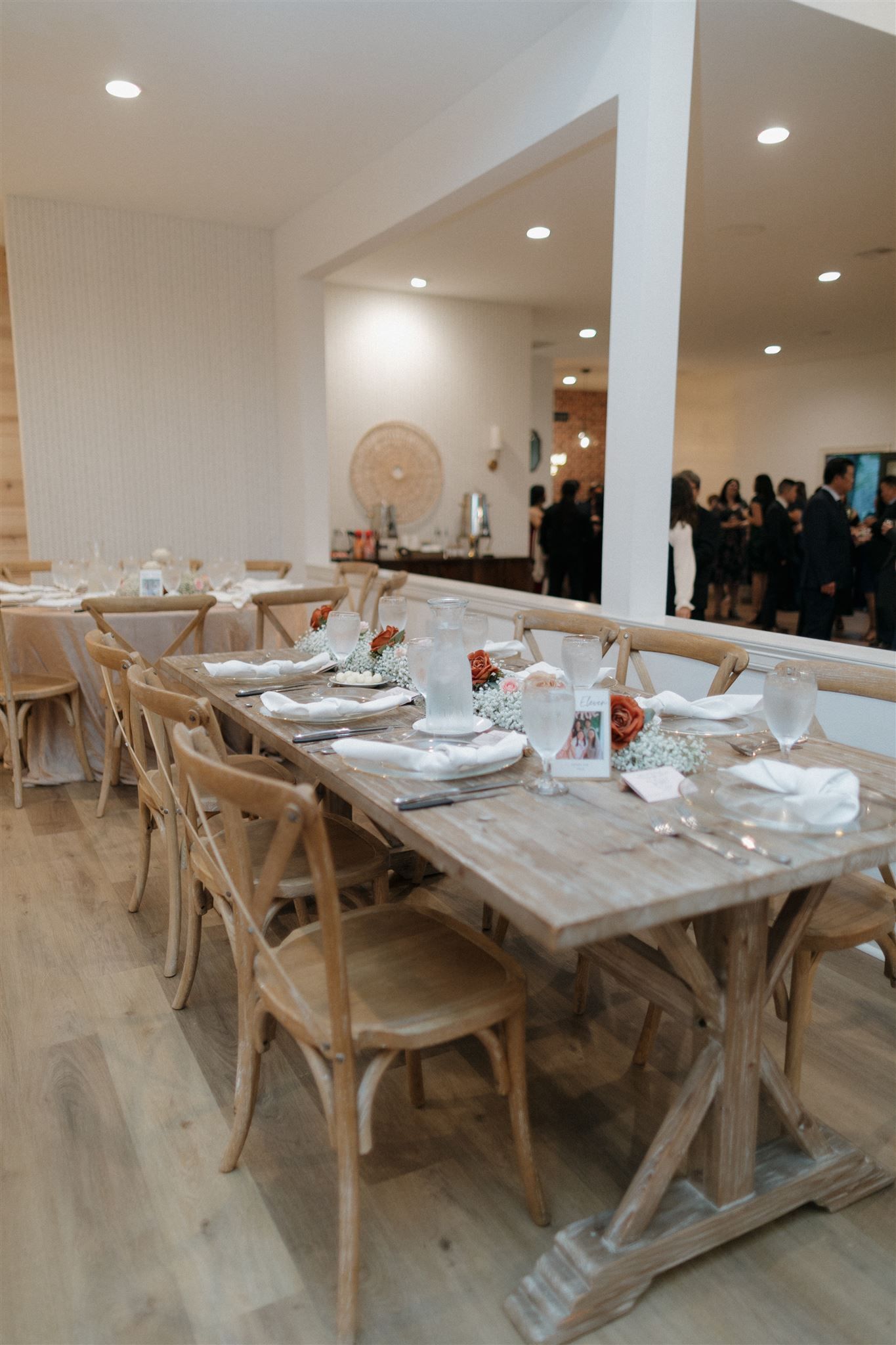 Long rustic farmhouse tables set for wedding reception with wooden chairs and white place settings.