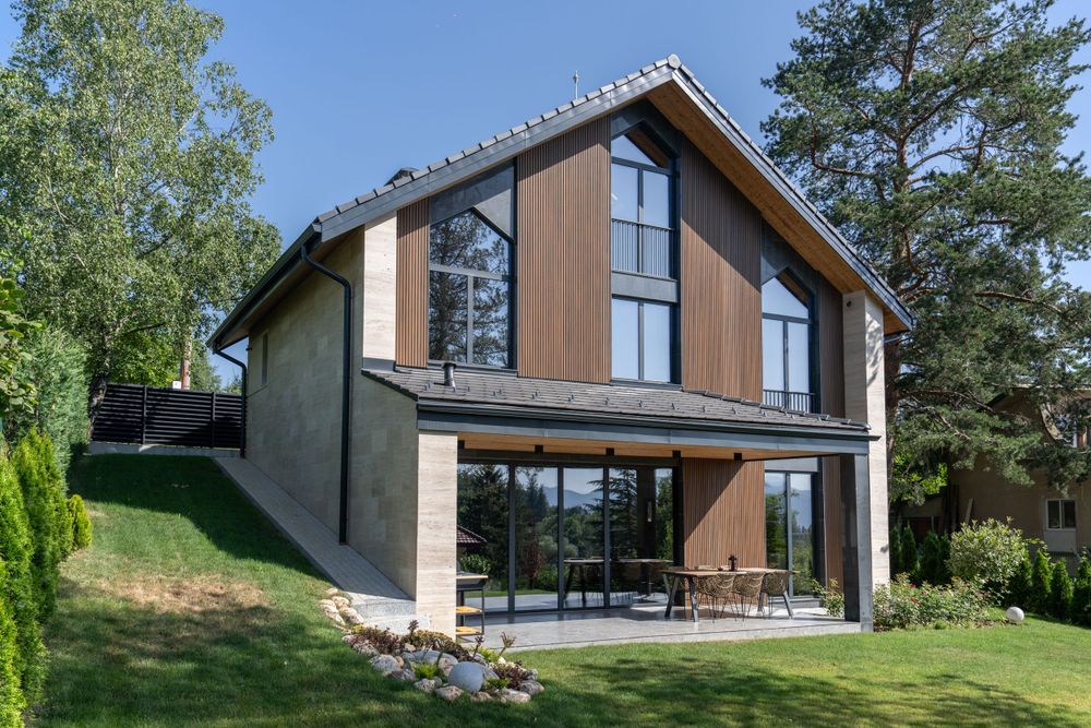 Modern wooden and concrete house exterior with large windows and sloped roof.