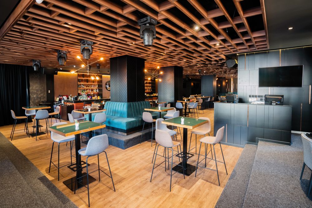 Contemporary restaurant space with wooden lattice ceiling, turquoise booths, and high-top tables.