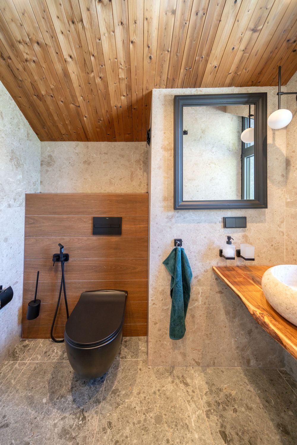 Modern bathroom interior with wooden ceiling, black fixtures, and concrete flooring.