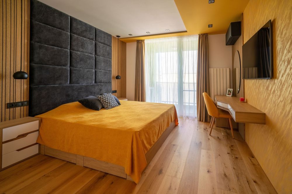 Contemporary bedroom with yellow accent wall, padded headboard, and wooden flooring.