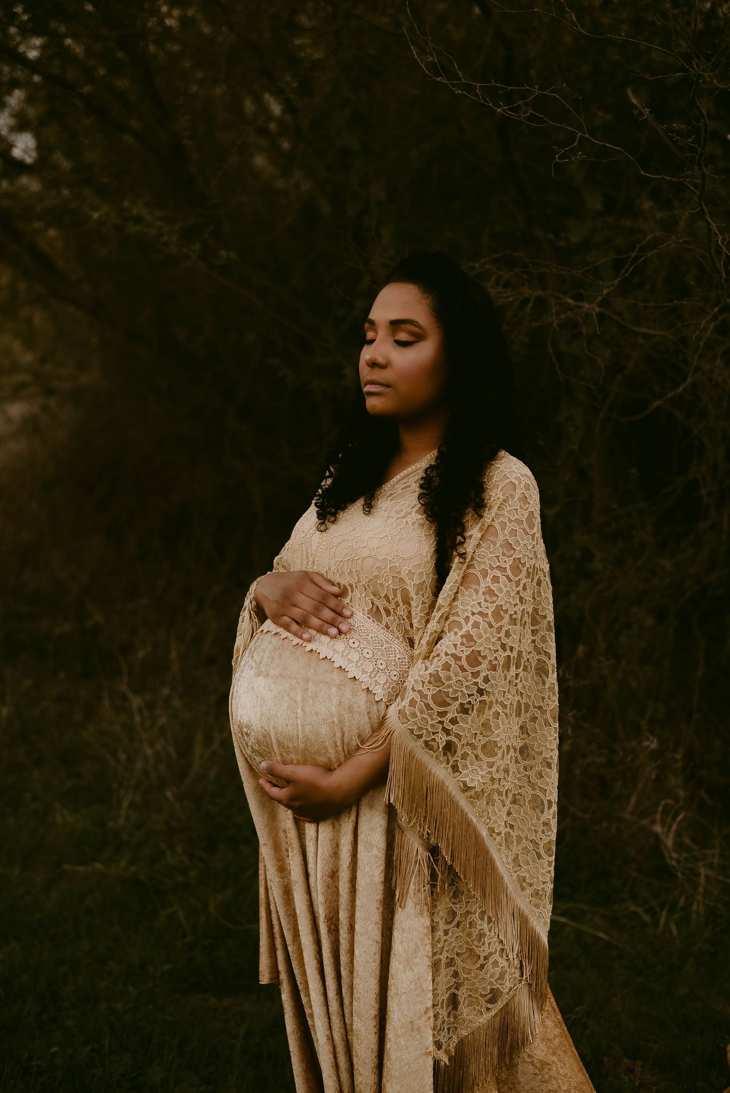 Ethereal maternity portrait with elegant lace shawl against dark forest backdrop.