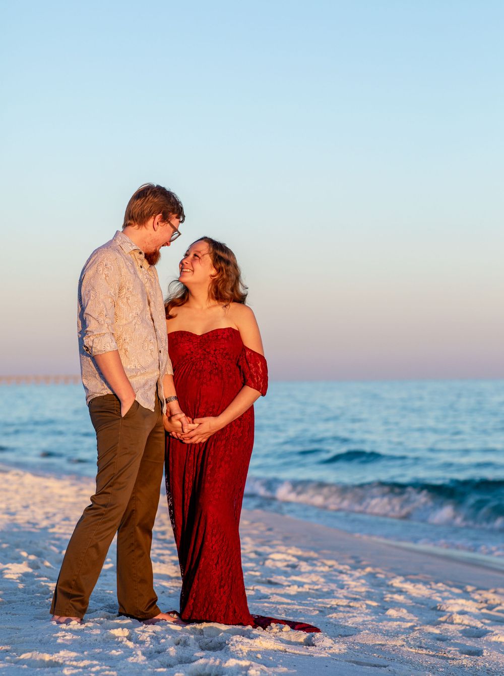 Romantic beach sunset photo with couple in red dress and casual attire.