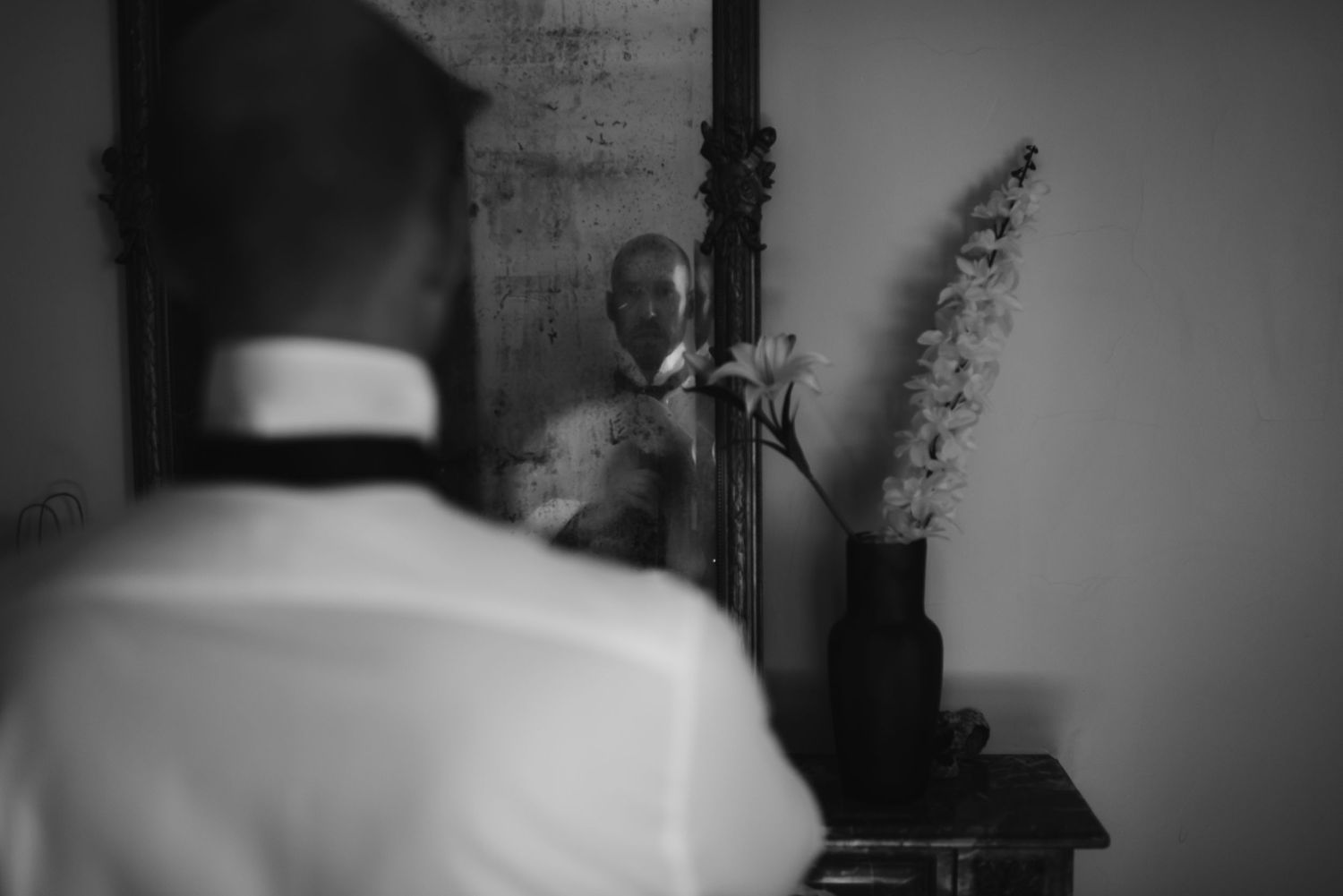 Black and white reflection of a man adjusting his tie in a mirror.