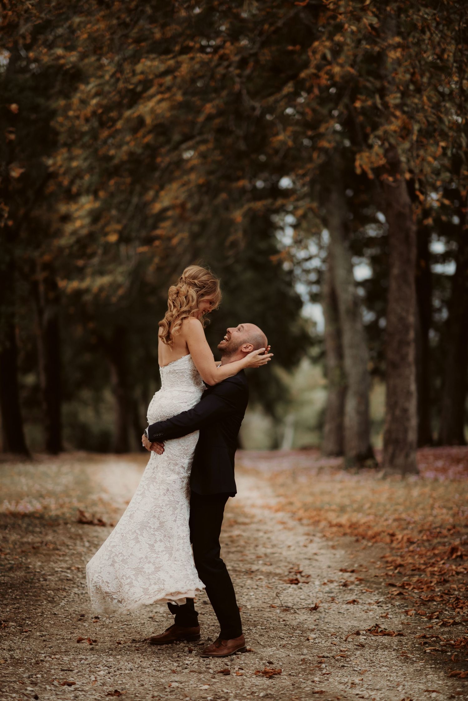 Romantic wedding dance beneath autumn trees on leaf-covered path.