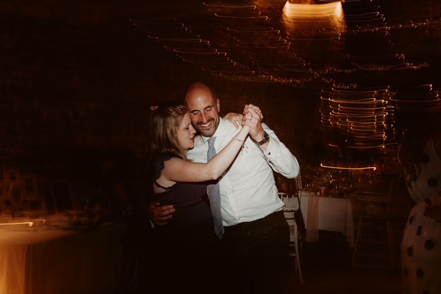 A couple dances in warm lighting during their wedding reception in a rustic stone venue.