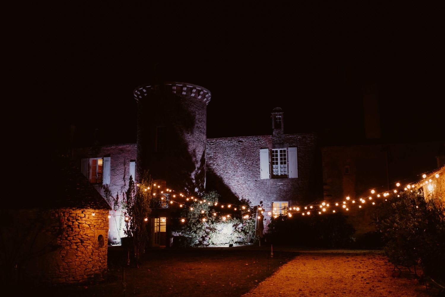 A stone castle illuminated by string lights at night creates a romantic wedding venue atmosphere.
