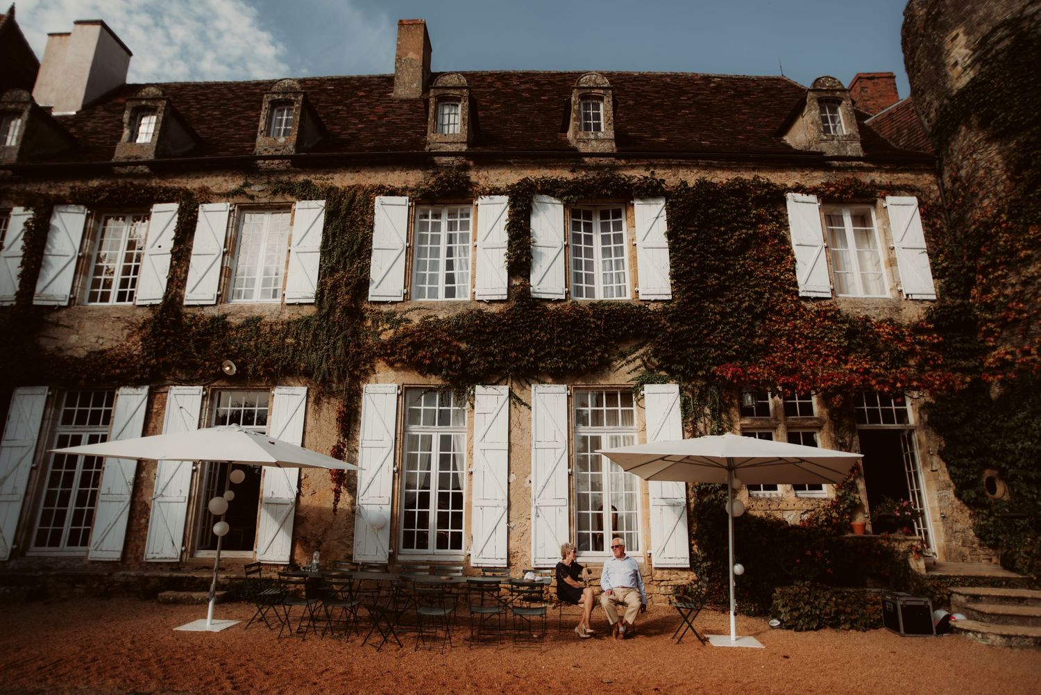 Elegant French chateau with white shutters and ivy-covered walls in warm afternoon light.