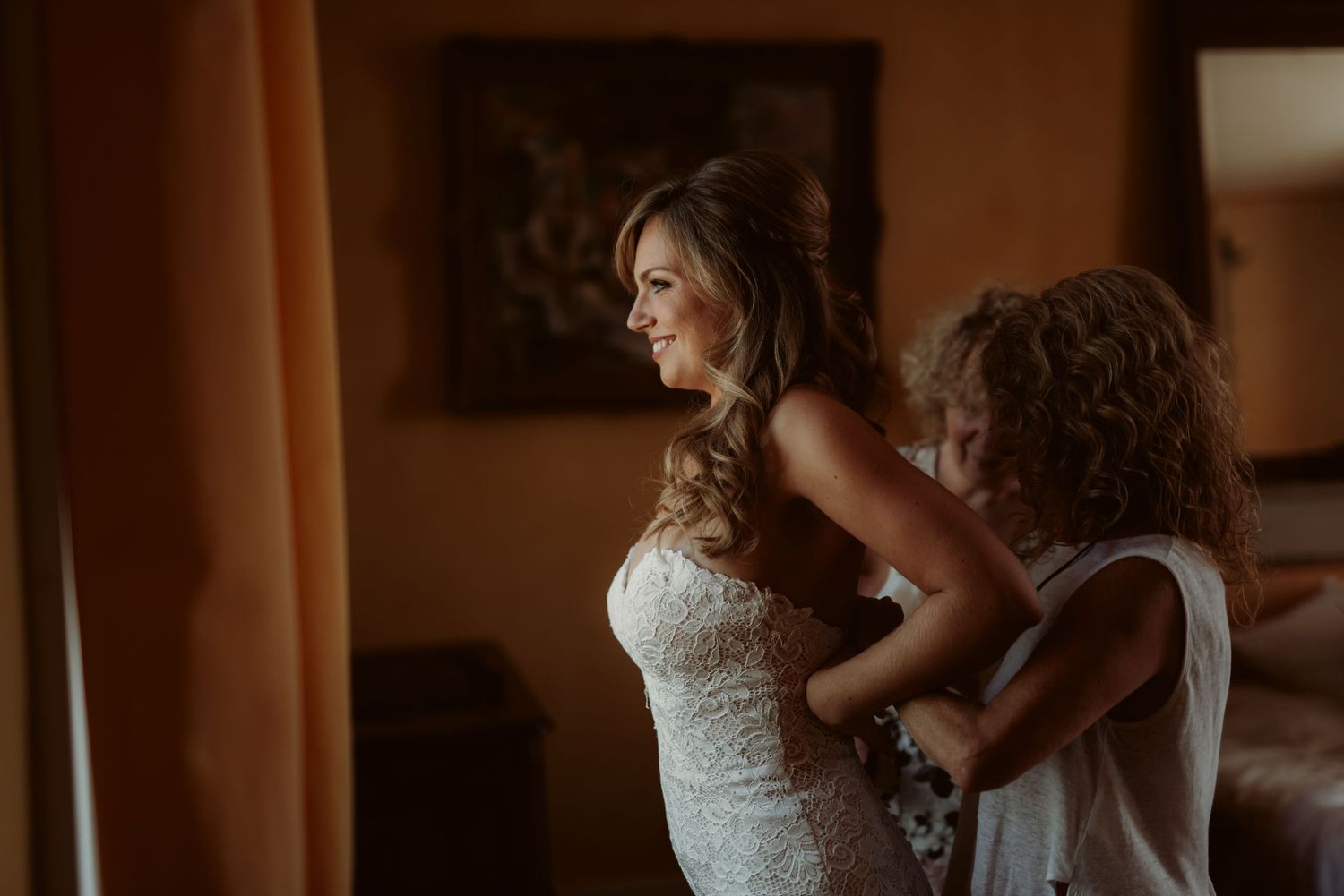 Warm-toned image of wedding dress fitting in sunlit room.