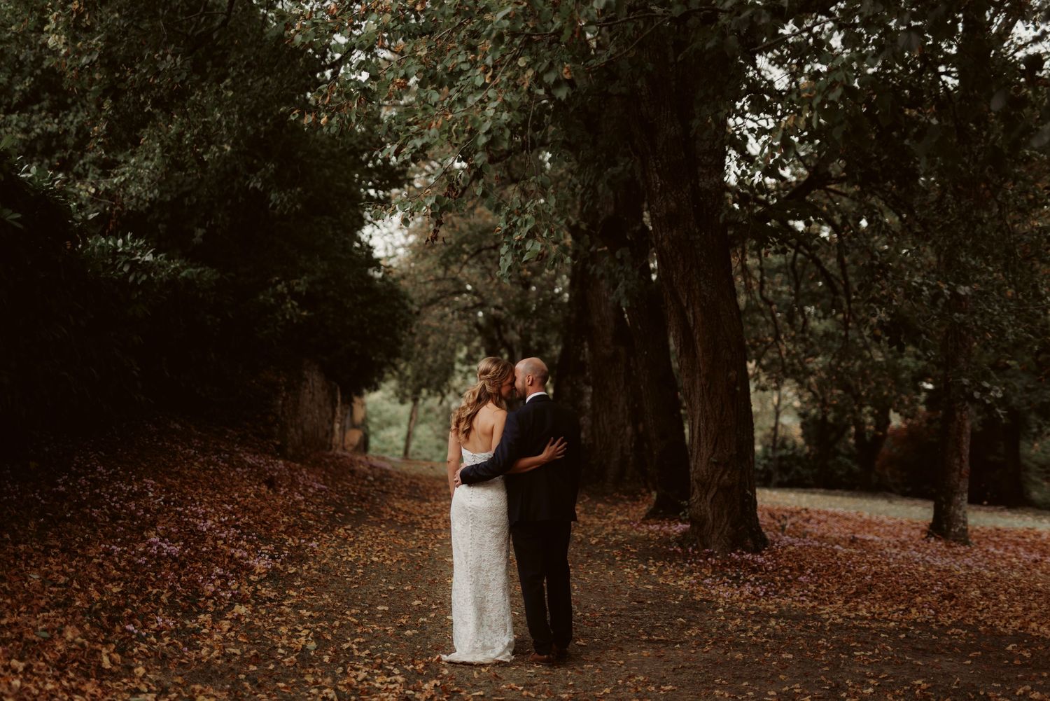Couple embraces on a romantic forest path covered in autumn leaves.