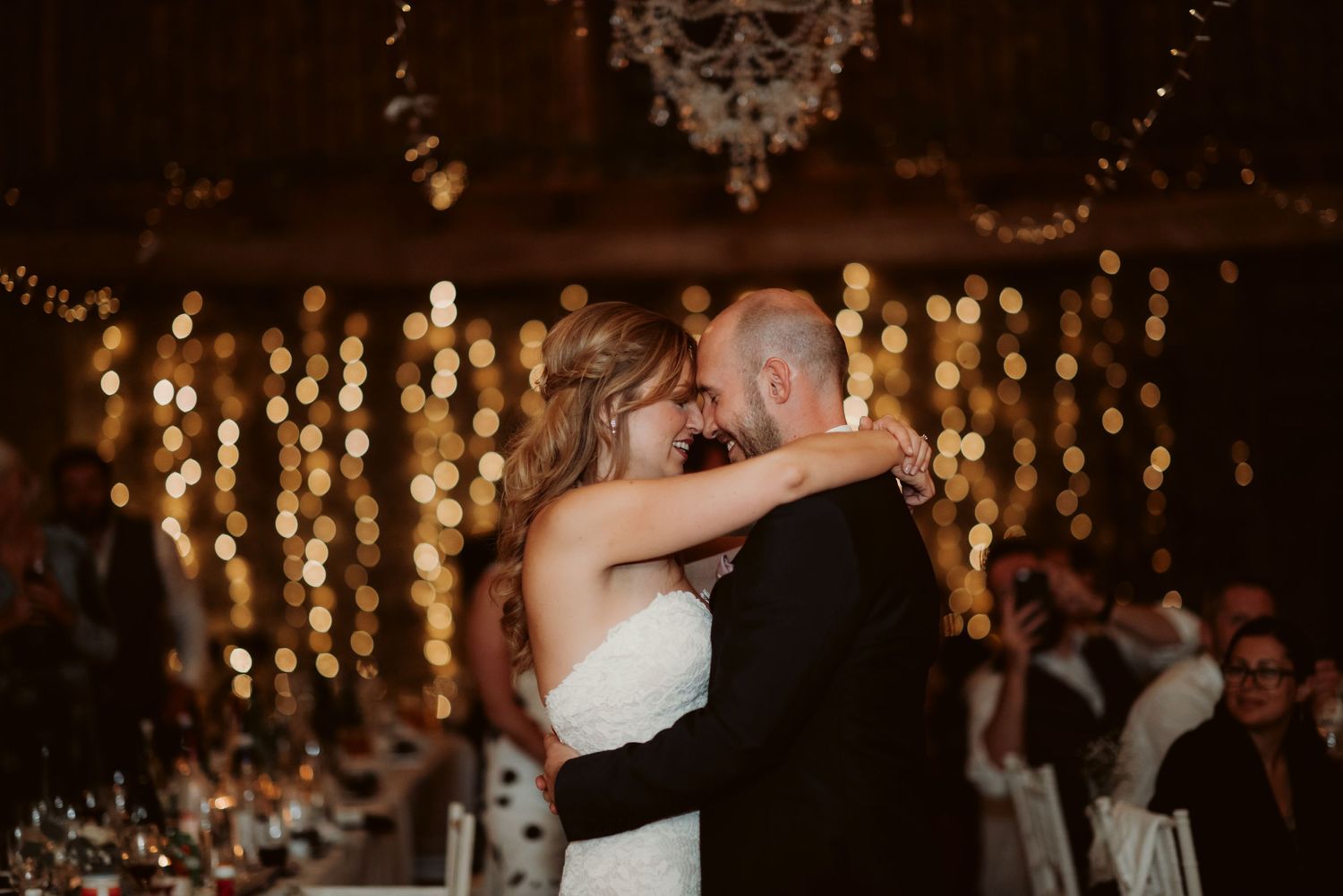 A couple shares an intimate dance moment under warm string lights at their wedding reception.