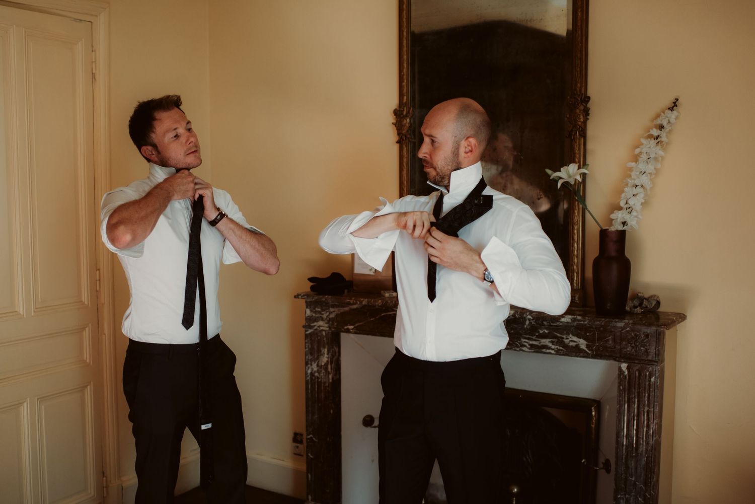 Two men in formal attire adjusting their neckties while getting ready.