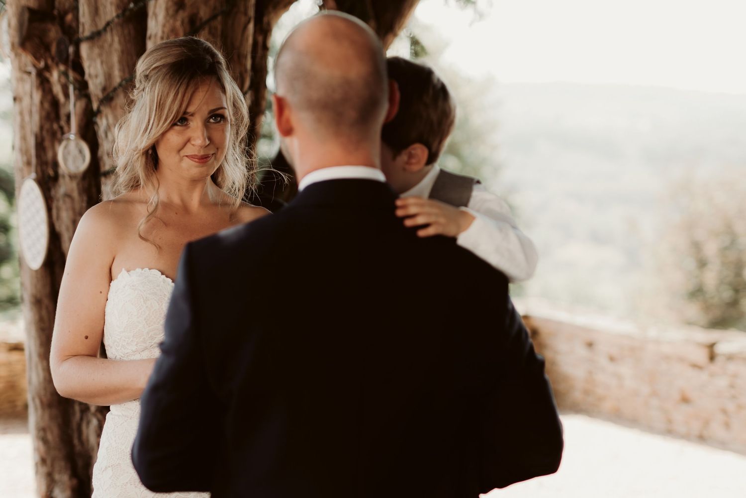 A heartfelt wedding ceremony moment captured in warm sunlight under trees.
